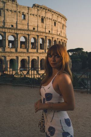 A person in a floral dress poses at sunset in front of the historic Roman Colosseum in Italy.