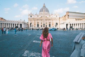 Tourist in pink dress admiring Saint Peter's Basilica and square at Vatican City in Rome.