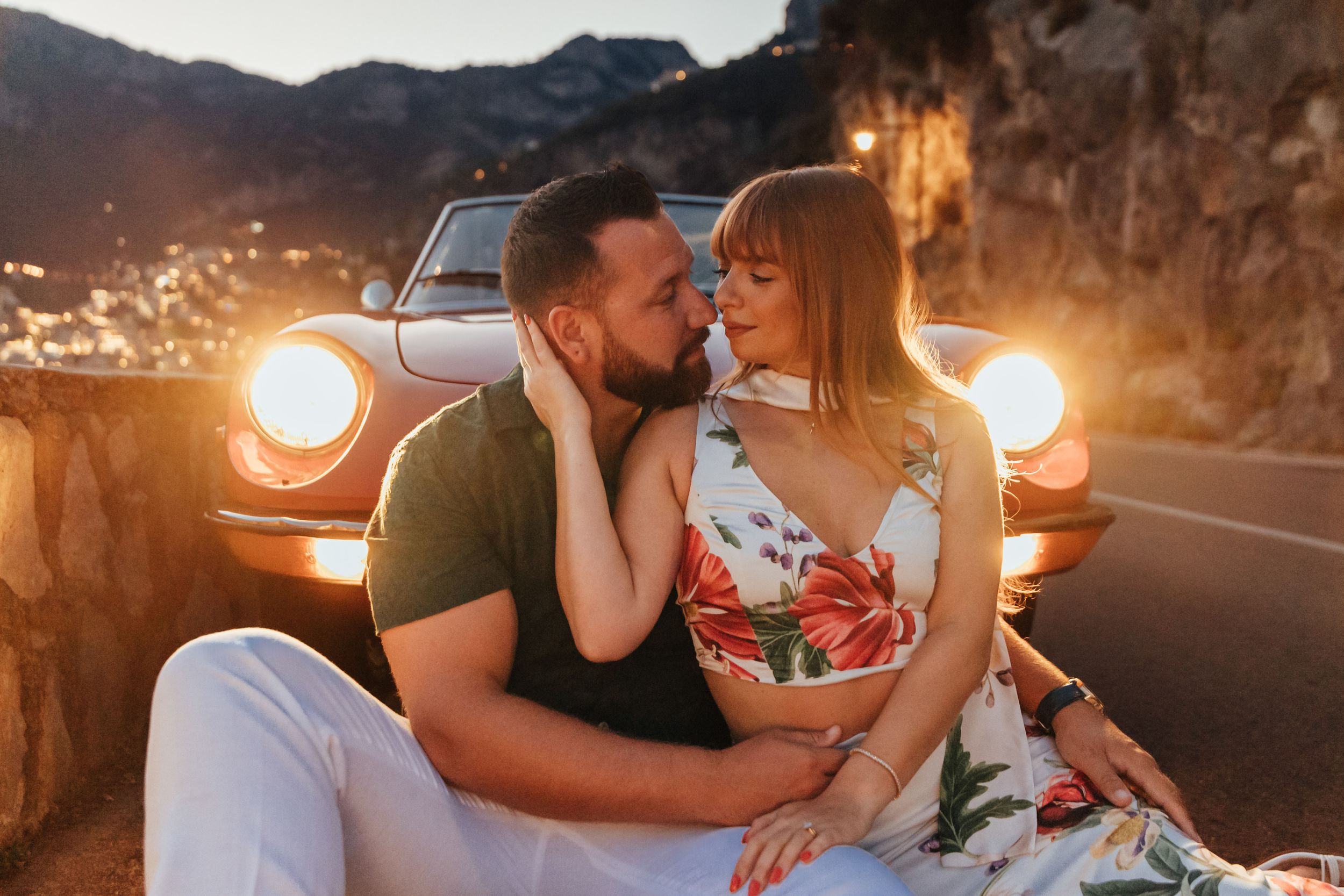 A romantic sunset date scene with a vintage orange car in the background on a mountain road.