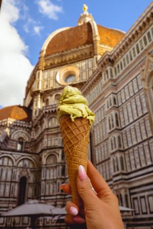 A pistachio gelato cone held up against the stunning backdrop of Florence's Duomo cathedral in Italy.