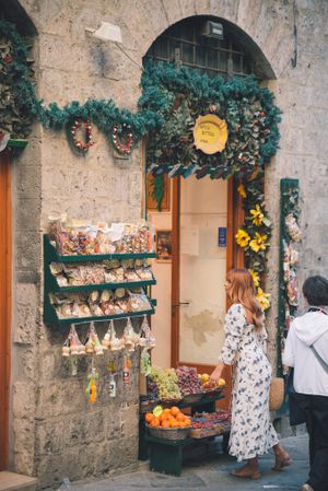 A charming storefront in Italy decorated with greenery and displaying fresh produce and local goods for sale.