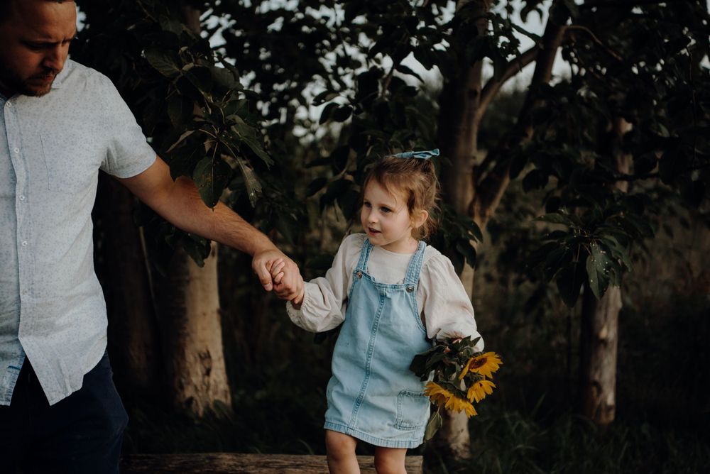 Adult and child walking together holding hands with sunflowers.