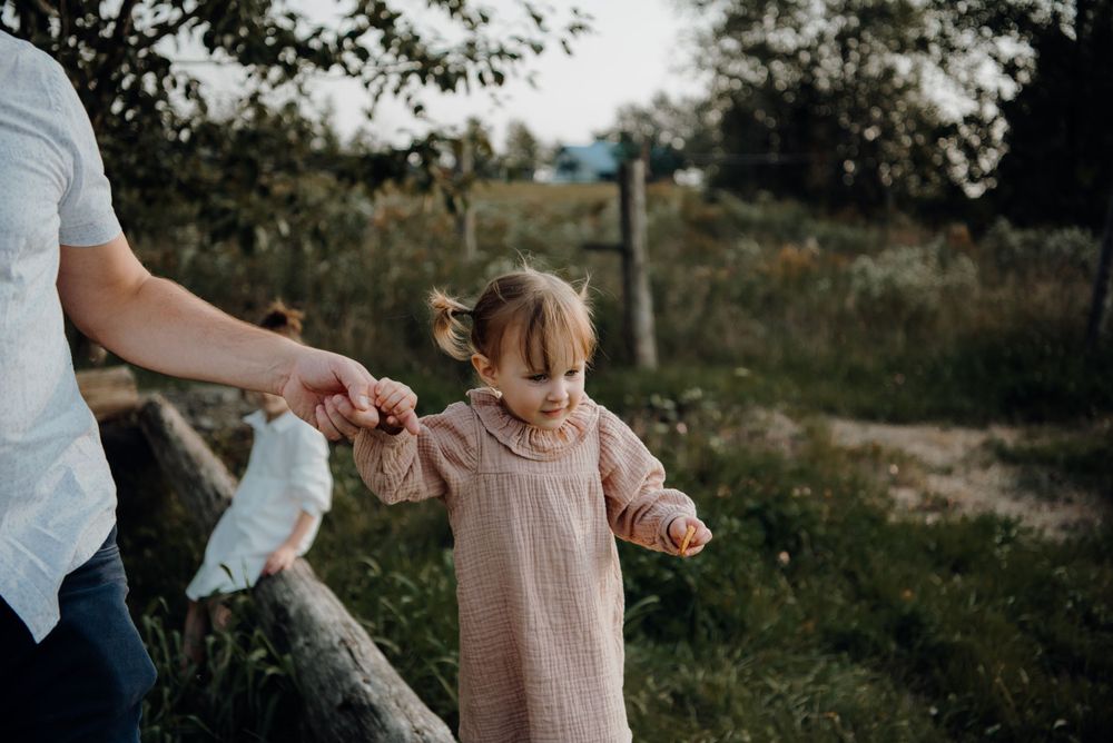 Child walking while holding adult's hand in rural outdoor setting.