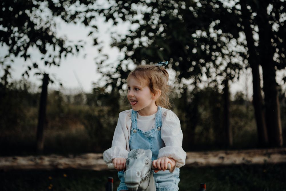 A small child in denim overalls plays outdoors among trees at twilight.
