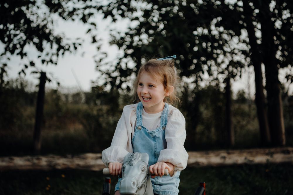 A joyful child in blue overalls and white shirt plays outside in a natural setting.