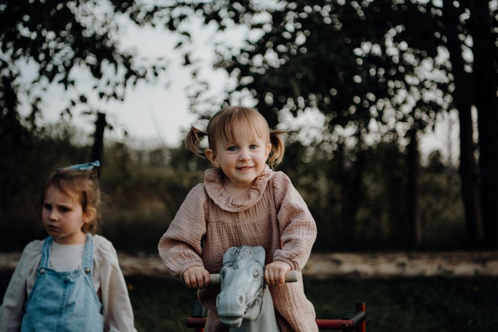 Children enjoy playtime on a rocking horse toy in an outdoor setting.
