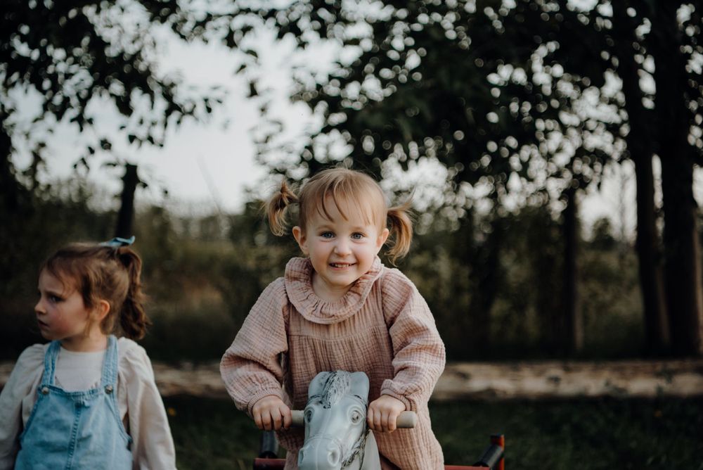 Two children playing outdoors with a rocking toy against a backdrop of trees.