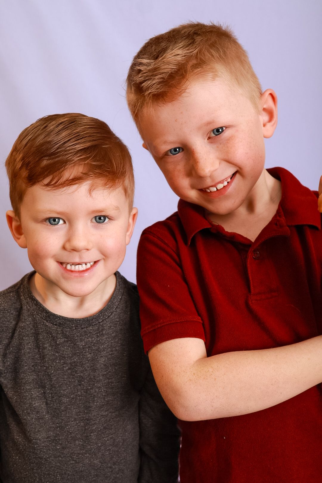 Two children in red and gray shirts pose together with bright smiles against a light background.