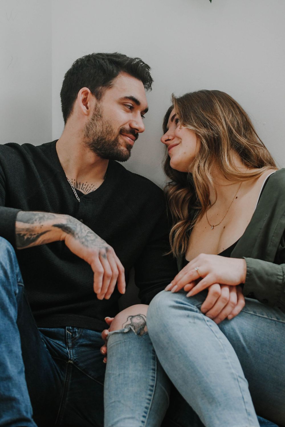 A romantic couple in casual wear share an intimate moment wearing jeans and dark sweaters while sitting close together.