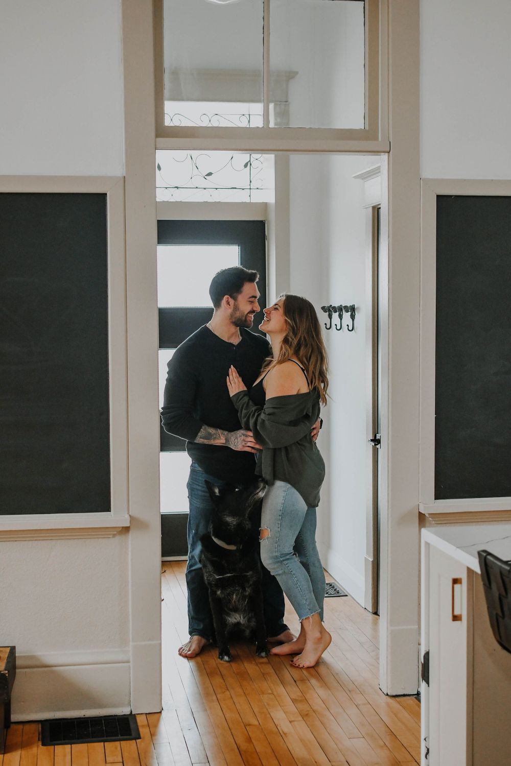 A couple shares an intimate moment in a doorway at home while their black dog sits patiently beside them.