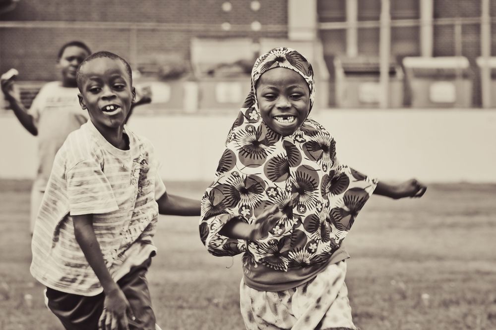 Group of smiling children playing and showing joy in an outdoor setting, captured in black and white photography.