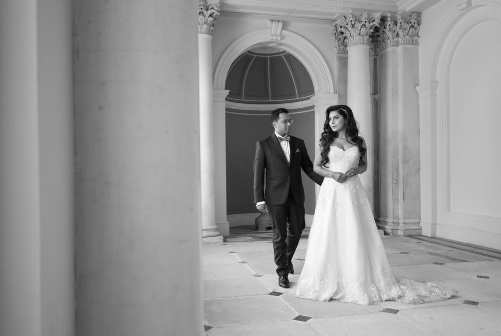 Black and white photo of a couple walking through an elegant archway with classical architecture.