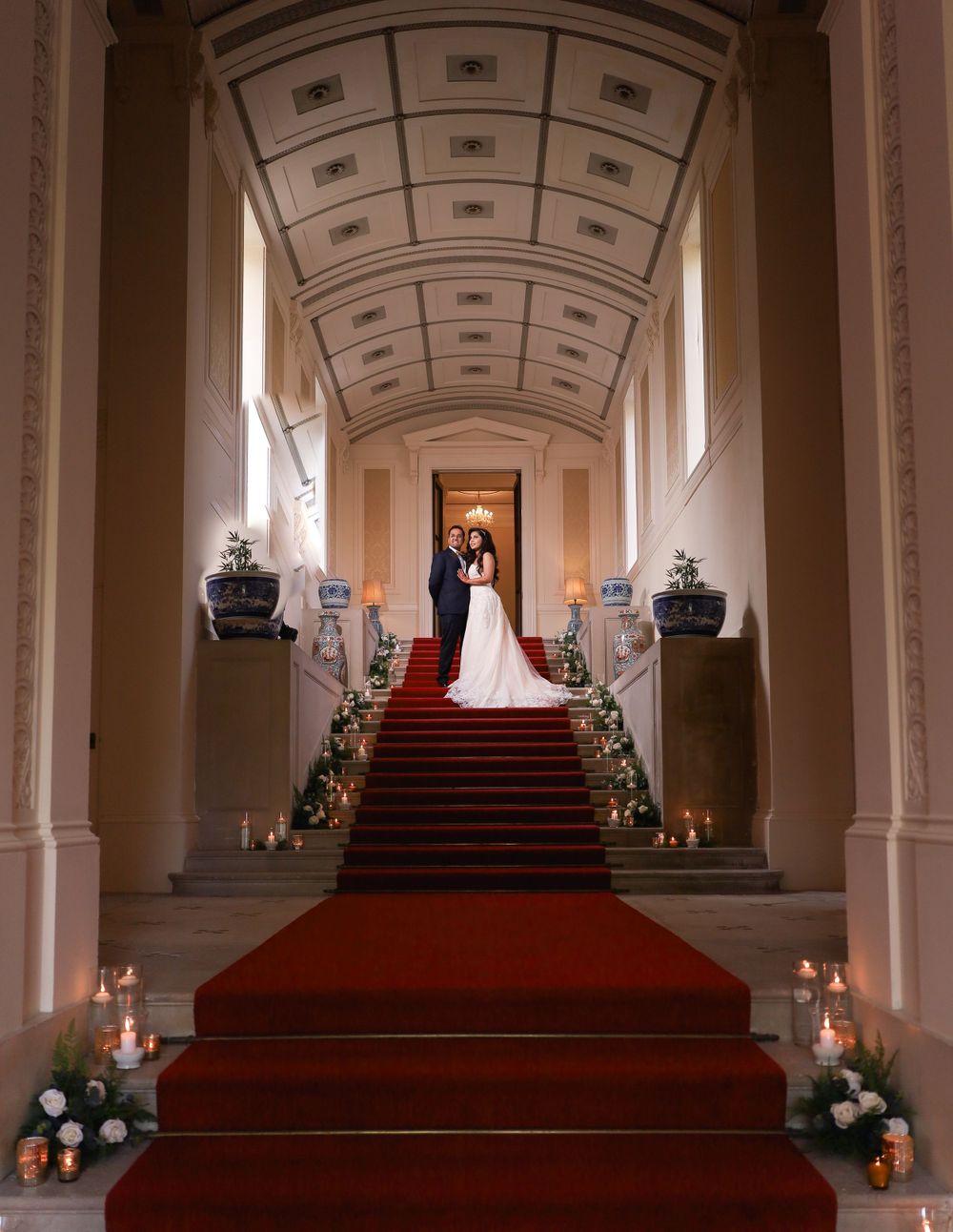 Grand staircase with red carpet and candles leading to an ornate hallway with coffered ceiling.