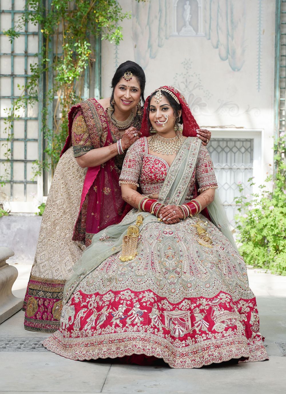 Two people wearing traditional Indian wedding attire with intricate embroidery and designs sitting in an outdoor setting. Shrubland Palace