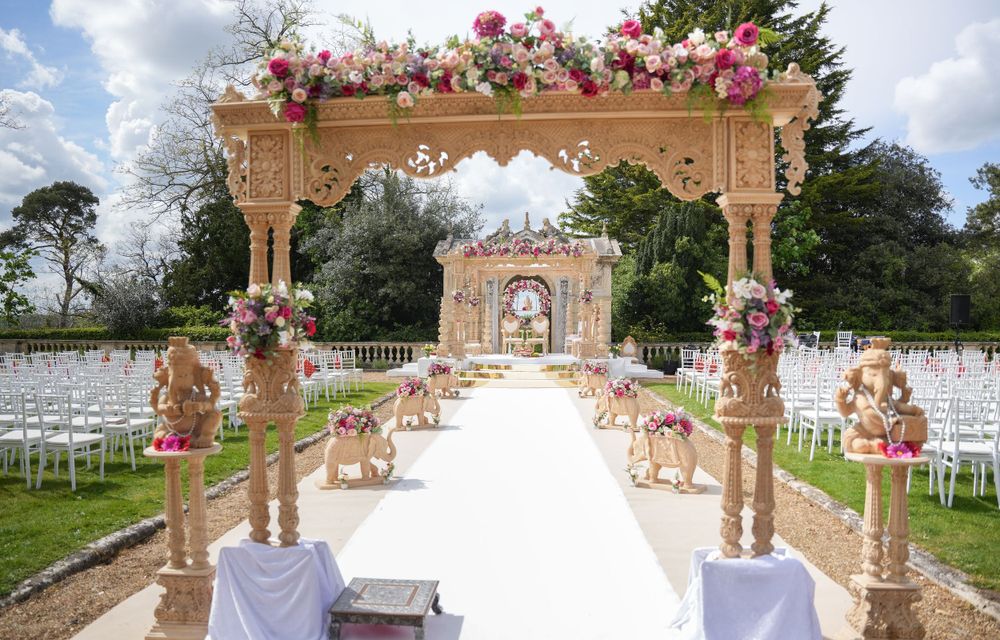 Elegant outdoor wedding ceremony setup with floral arch and white chairs along an aisle decorated with pink roses.
