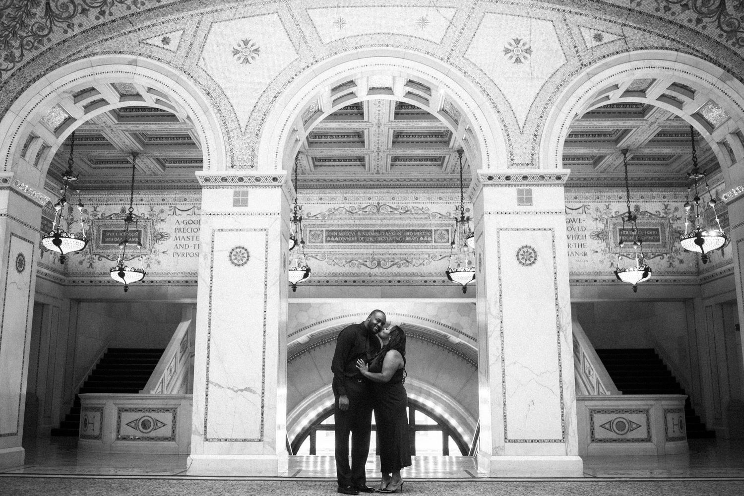 A romantic couple embraces in an elegant historic building with ornate white marble arches and classical architectural details.