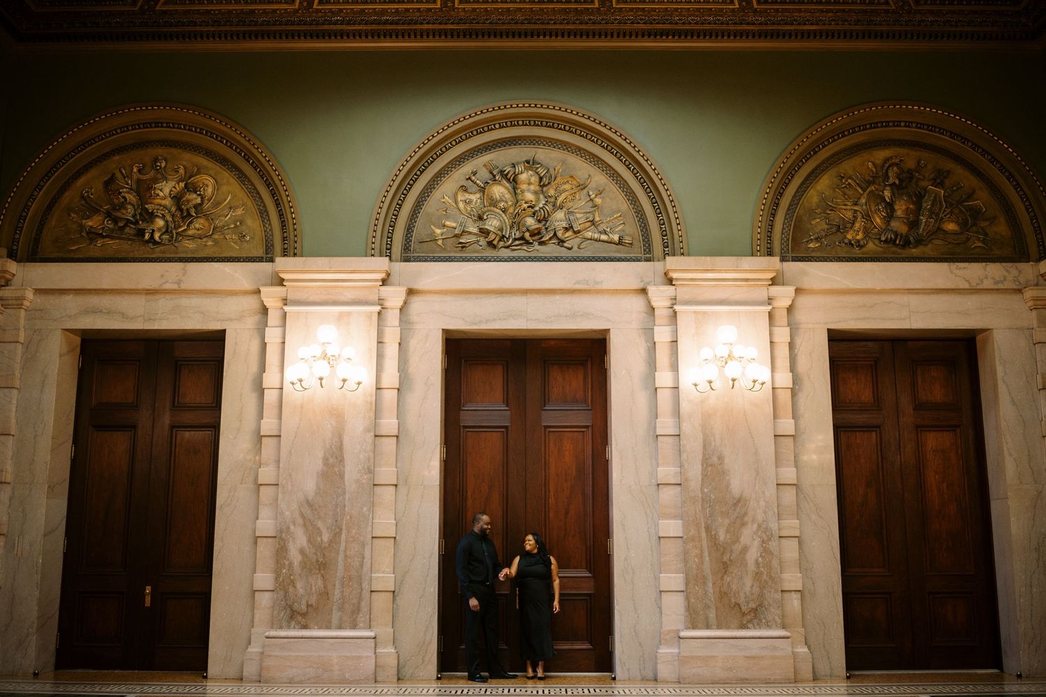 Elegant wooden doors with ornate architectural details and marble columns in a grand historic building hallway.
