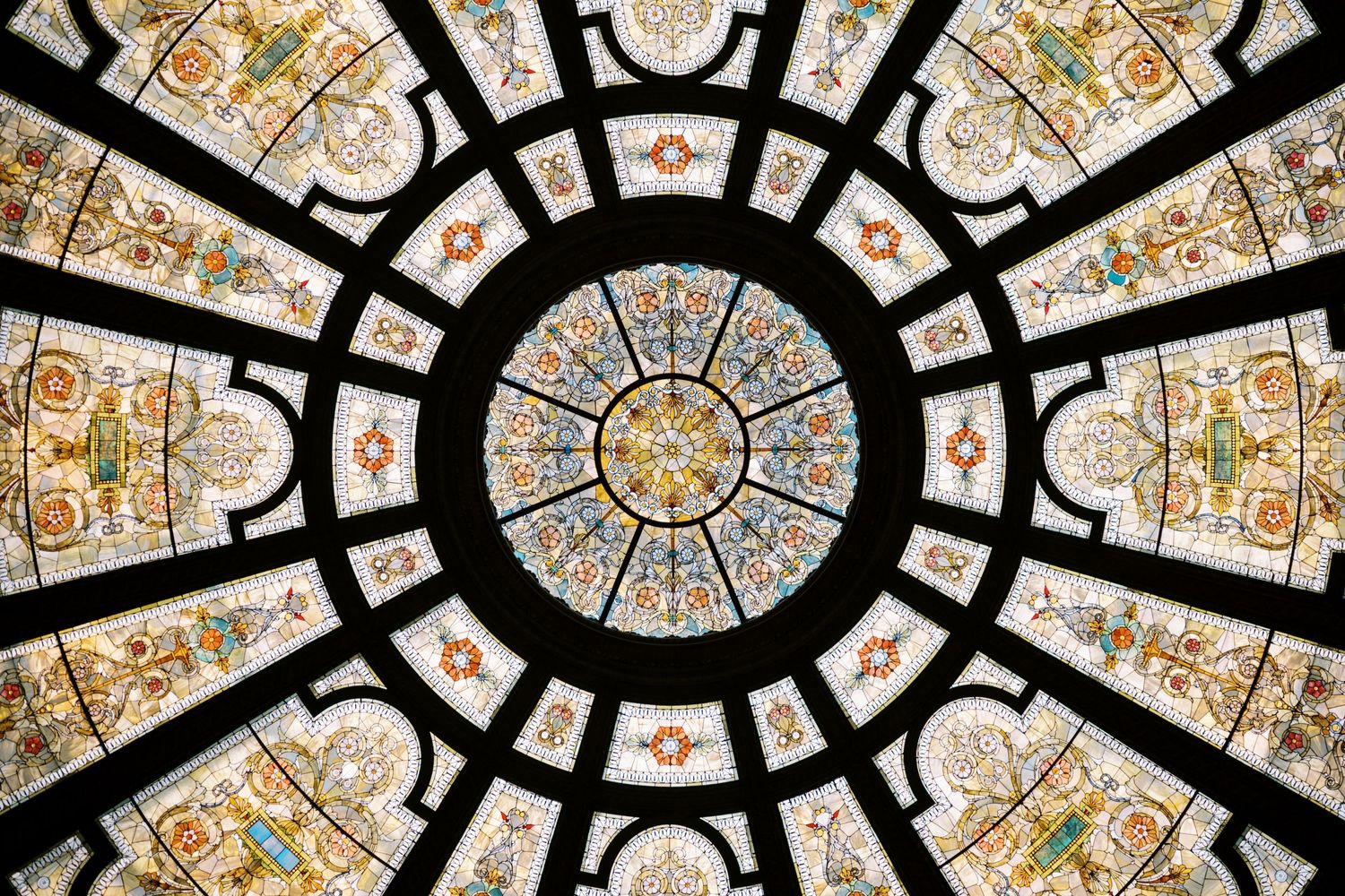 Ornate circular stained glass ceiling with intricate geometric patterns and floral motifs in beige and brown tones.