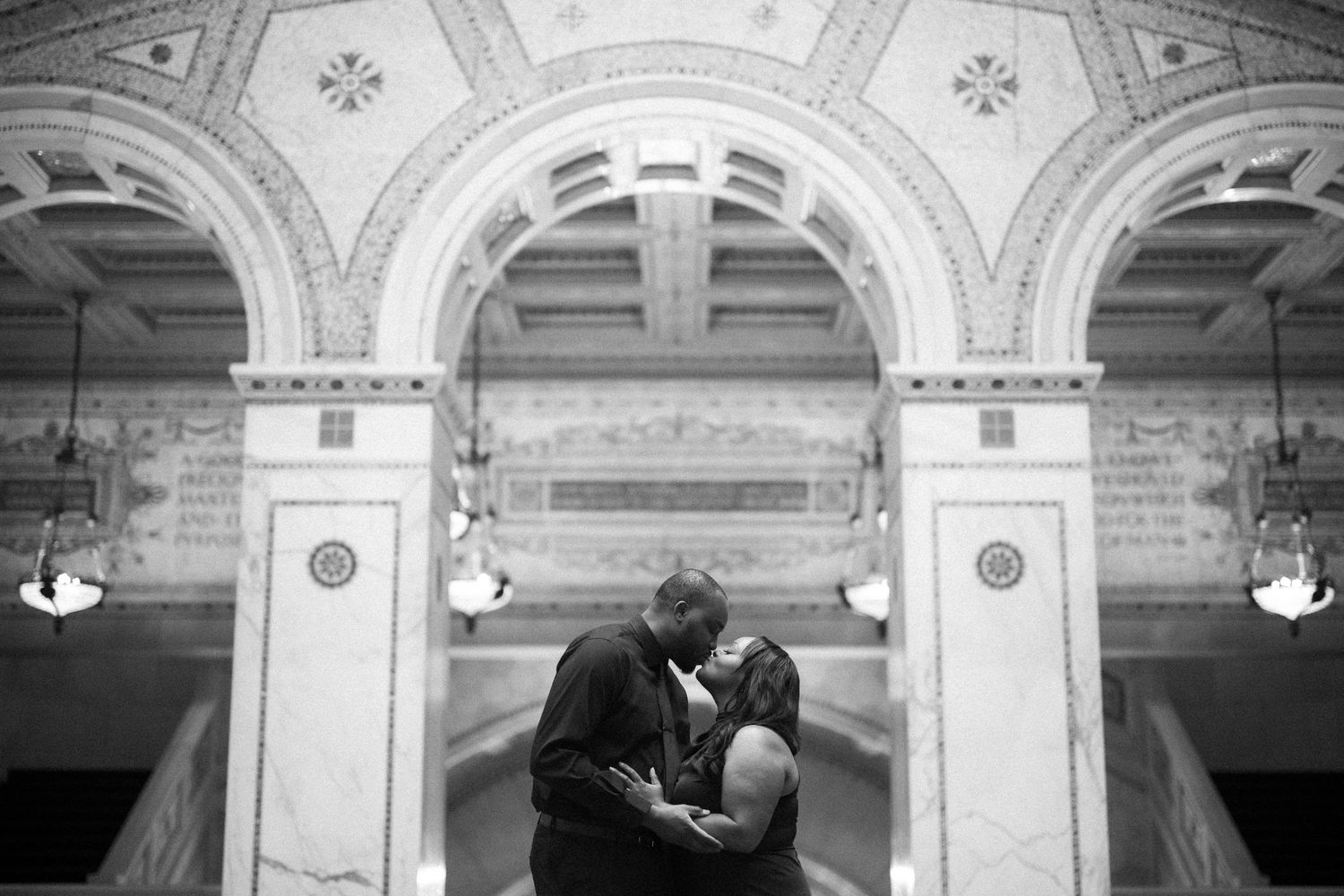 A romantic black and white moment captured under ornate archways with decorative molding in a grand historic building.