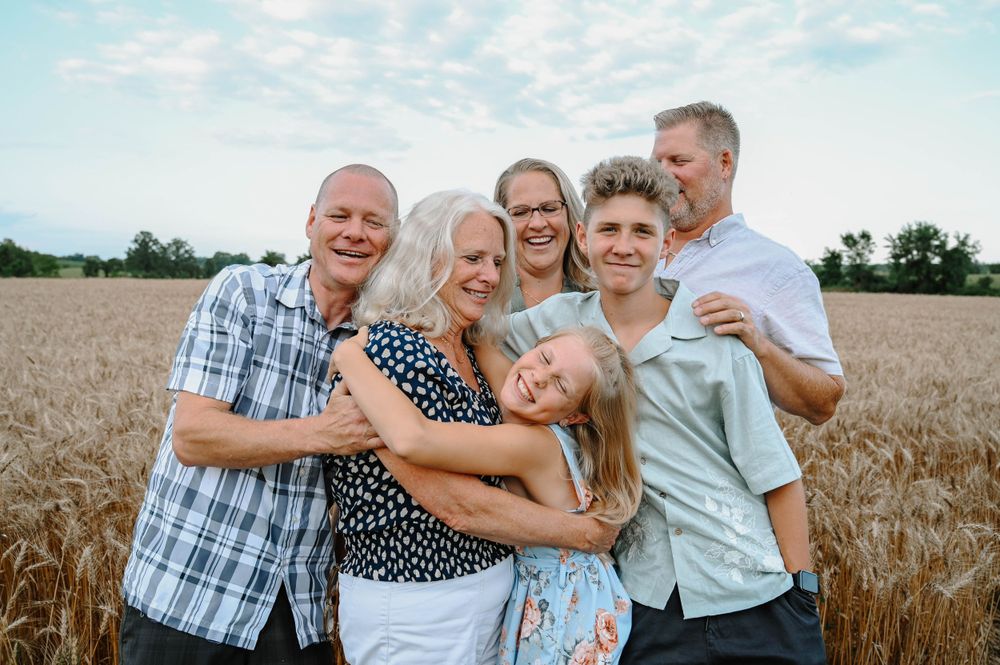 Family smiling and embracing together in a golden wheat field during sunset.