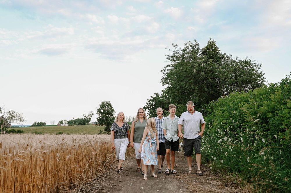 A group walks along a dirt path between tall wheat fields and green foliage on a sunny summer day.