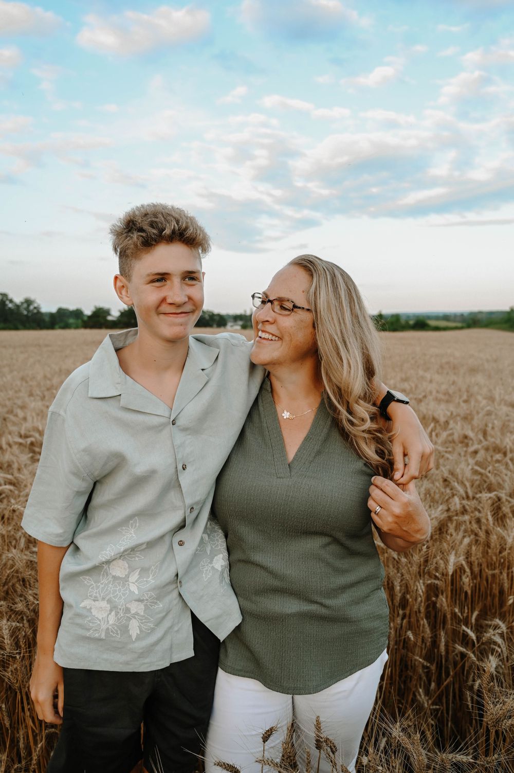 Two people share an intimate moment while standing in a golden wheat field under a cloudy summer sky.