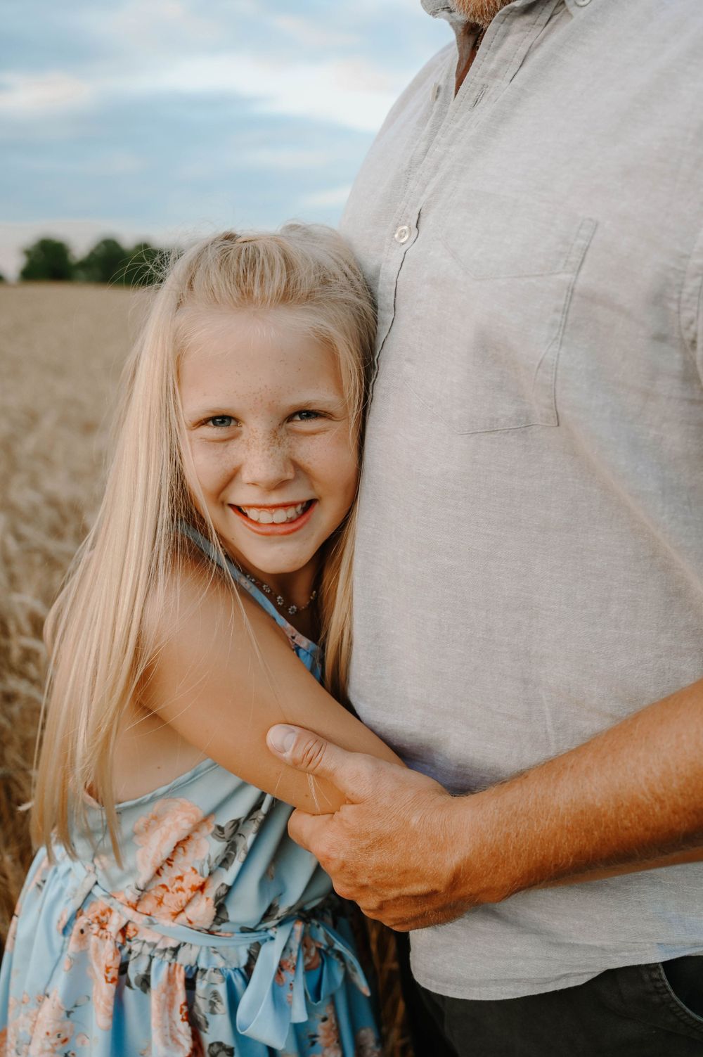 A touching moment captured in a wheat field showing a close embrace against a soft summer sky.