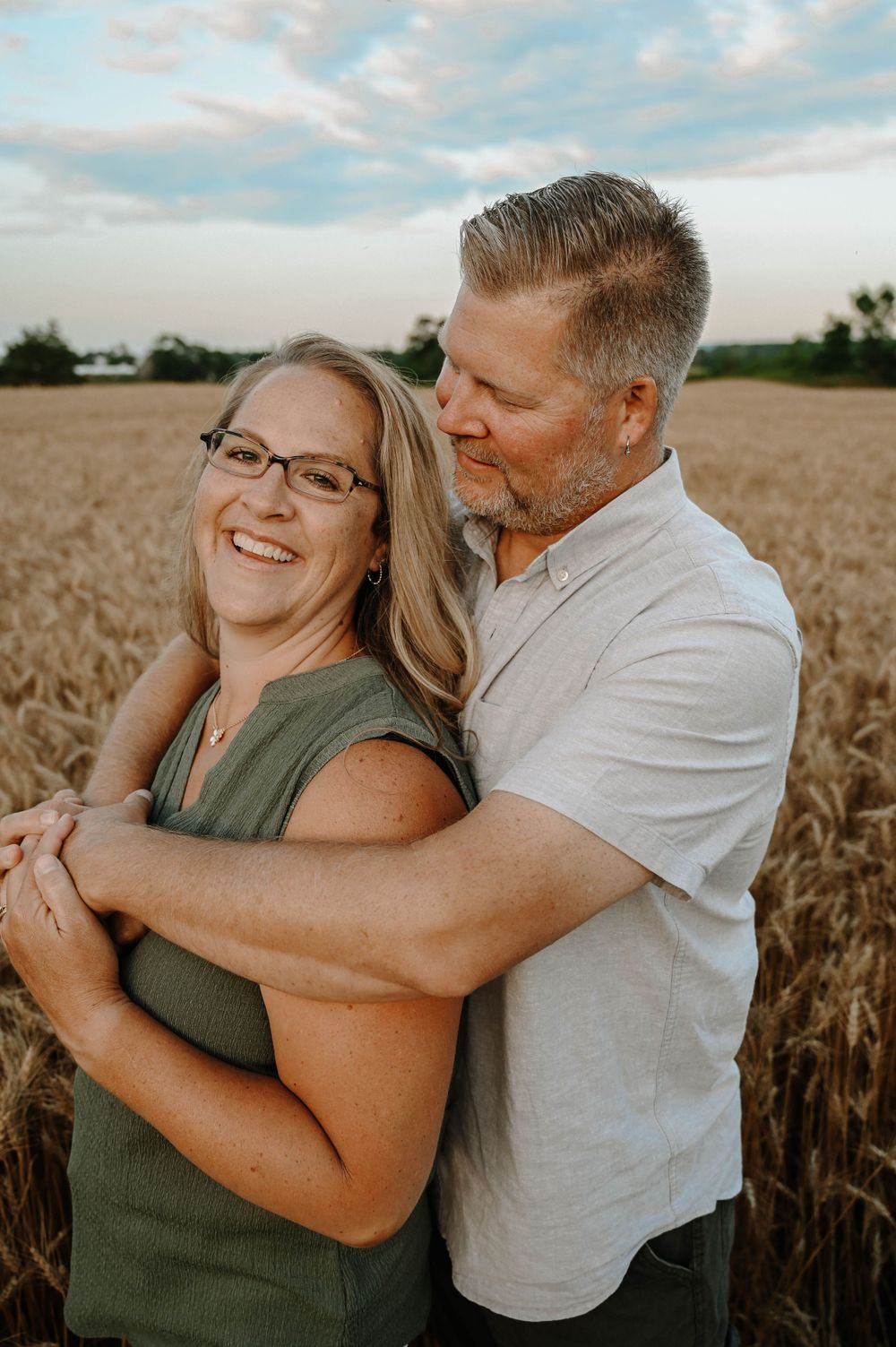 Happy couple embraces in wheat field at sunset during romantic photoshoot in countryside.