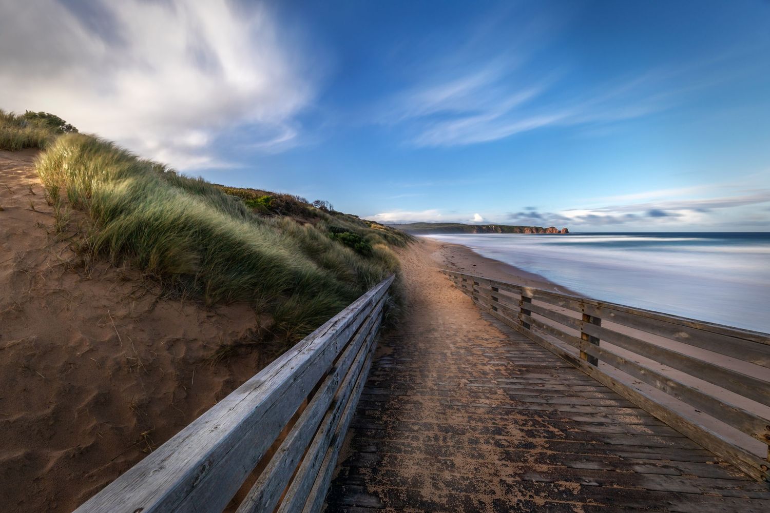 Wooden boardwalk along coastal dunes leads to beach under dramatic cloudy sky.