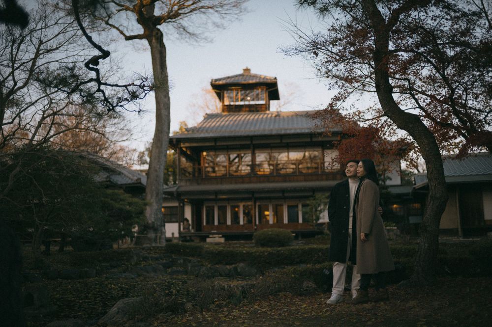 Couple standing in front of a traditional Japanese pagoda surrounded by autumn trees at dusk.