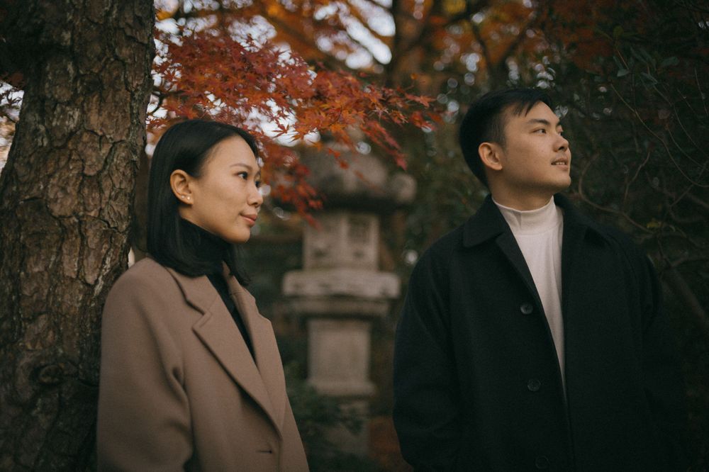 Couple standing by a tree with a stone lantern amid vibrant autumn foliage in Japan.
