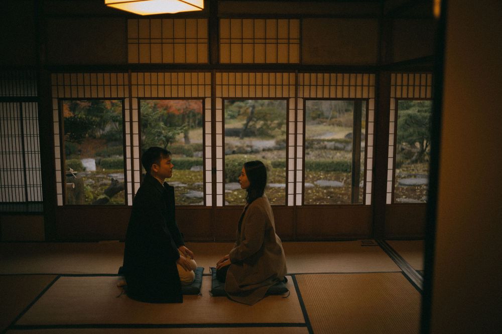 Couple sitting on tatami floor facing each other with a Japanese garden view through shoji screens.