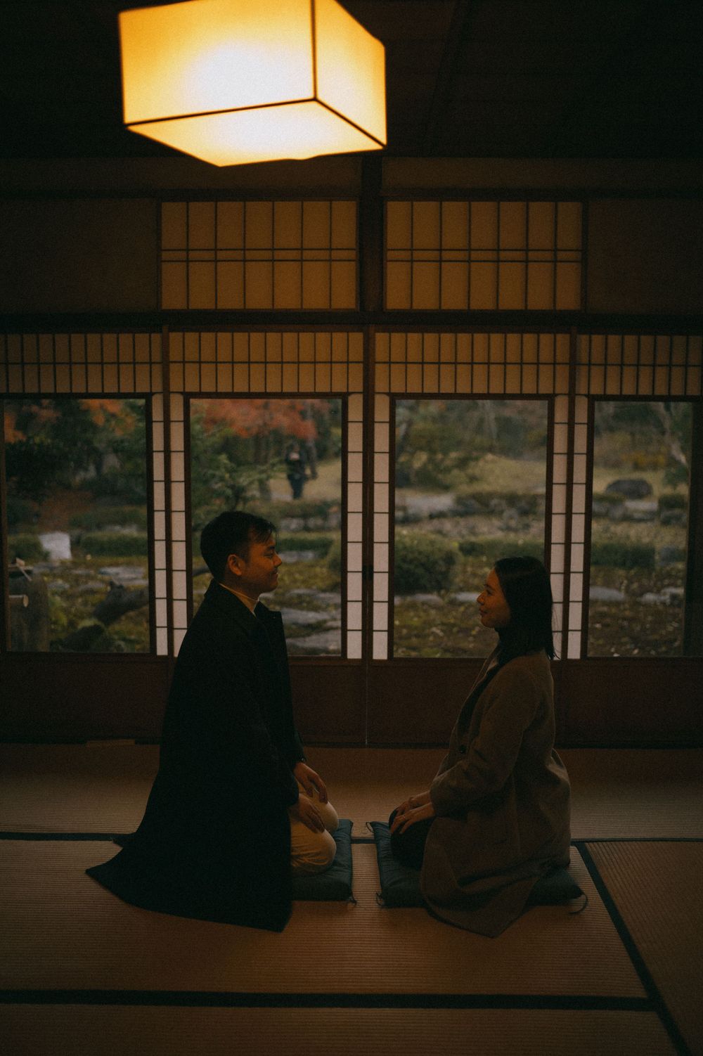 Couple seated on tatami mats in a dimly lit Japanese room with a glowing paper lantern above.