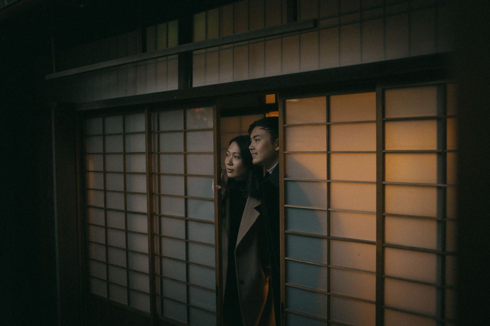 Couple peeking through a sliding shoji door in a traditional Japanese building at night.