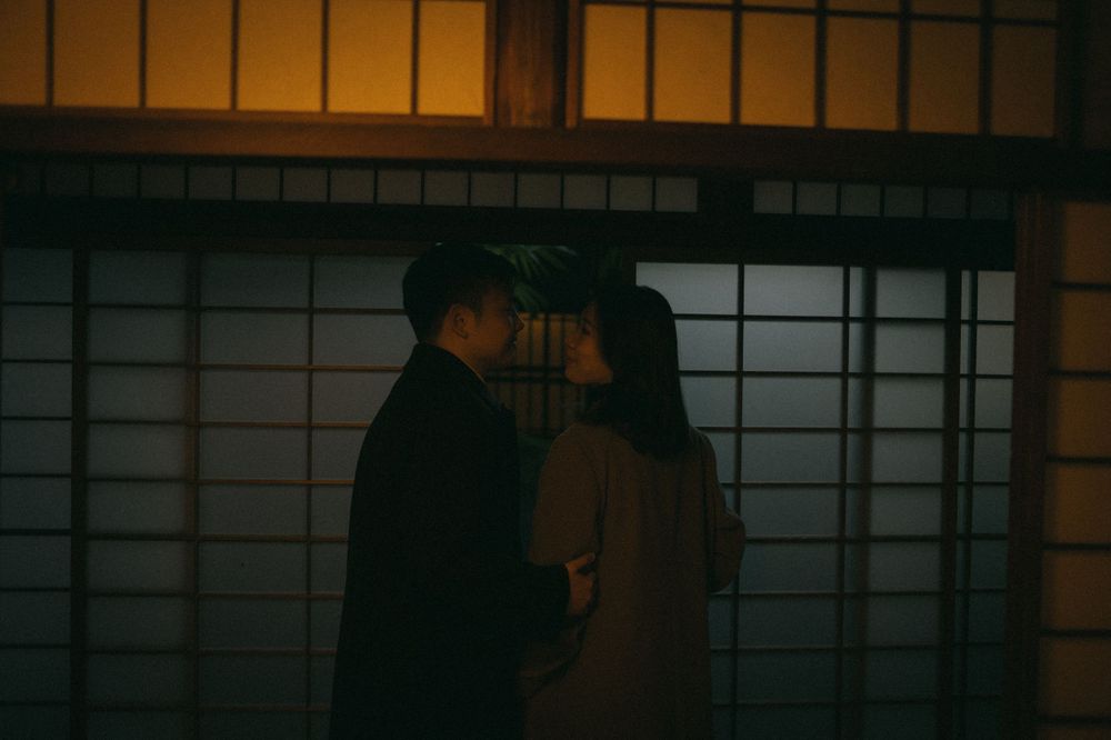 Couple sharing an intimate moment by glowing shoji screens in a dark traditional Japanese interior.