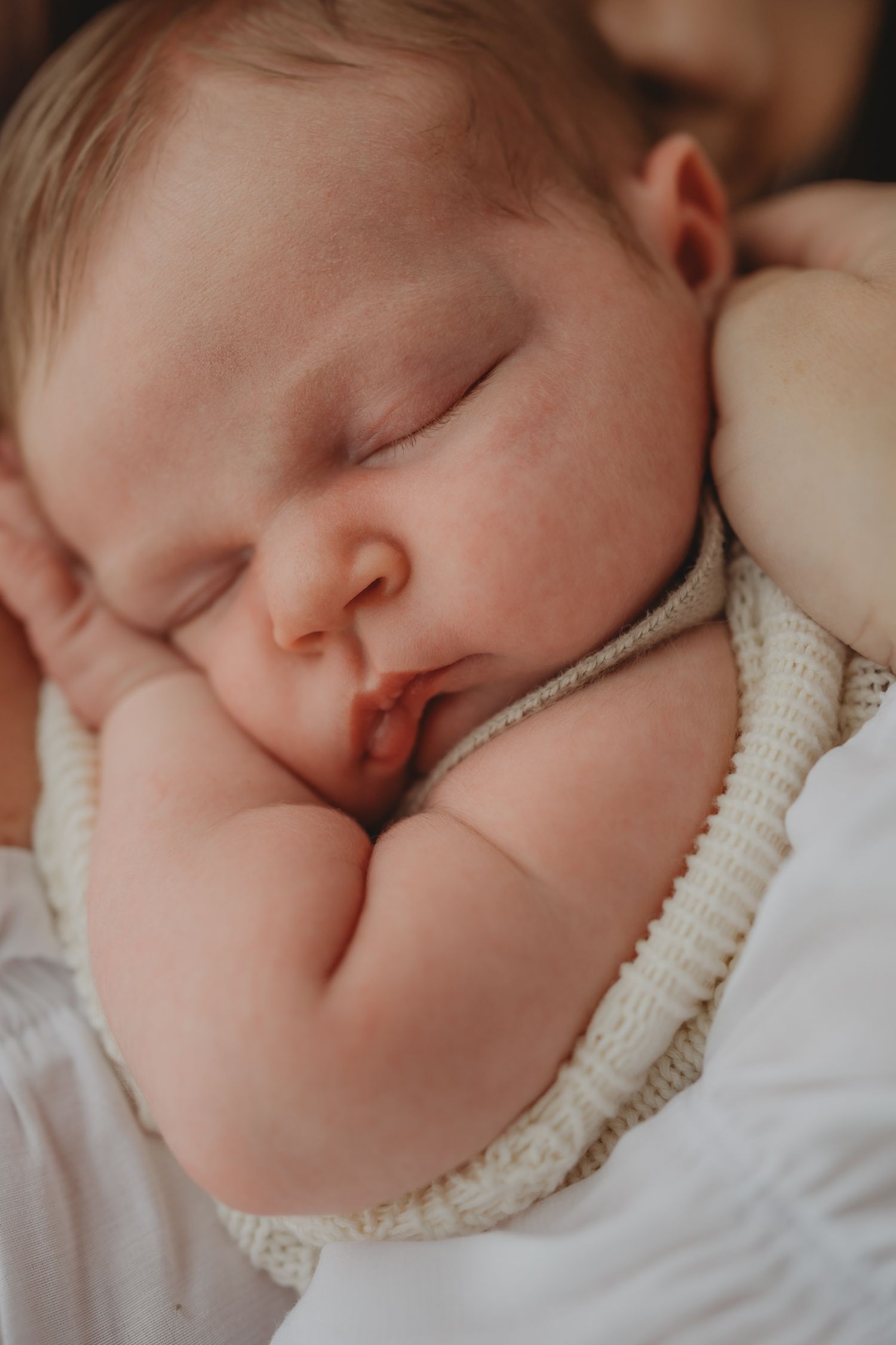 Sleeping baby peacefully rests wrapped in soft knit blanket in serene close-up portrait in my cosy newborn photography studio in Shepshed.