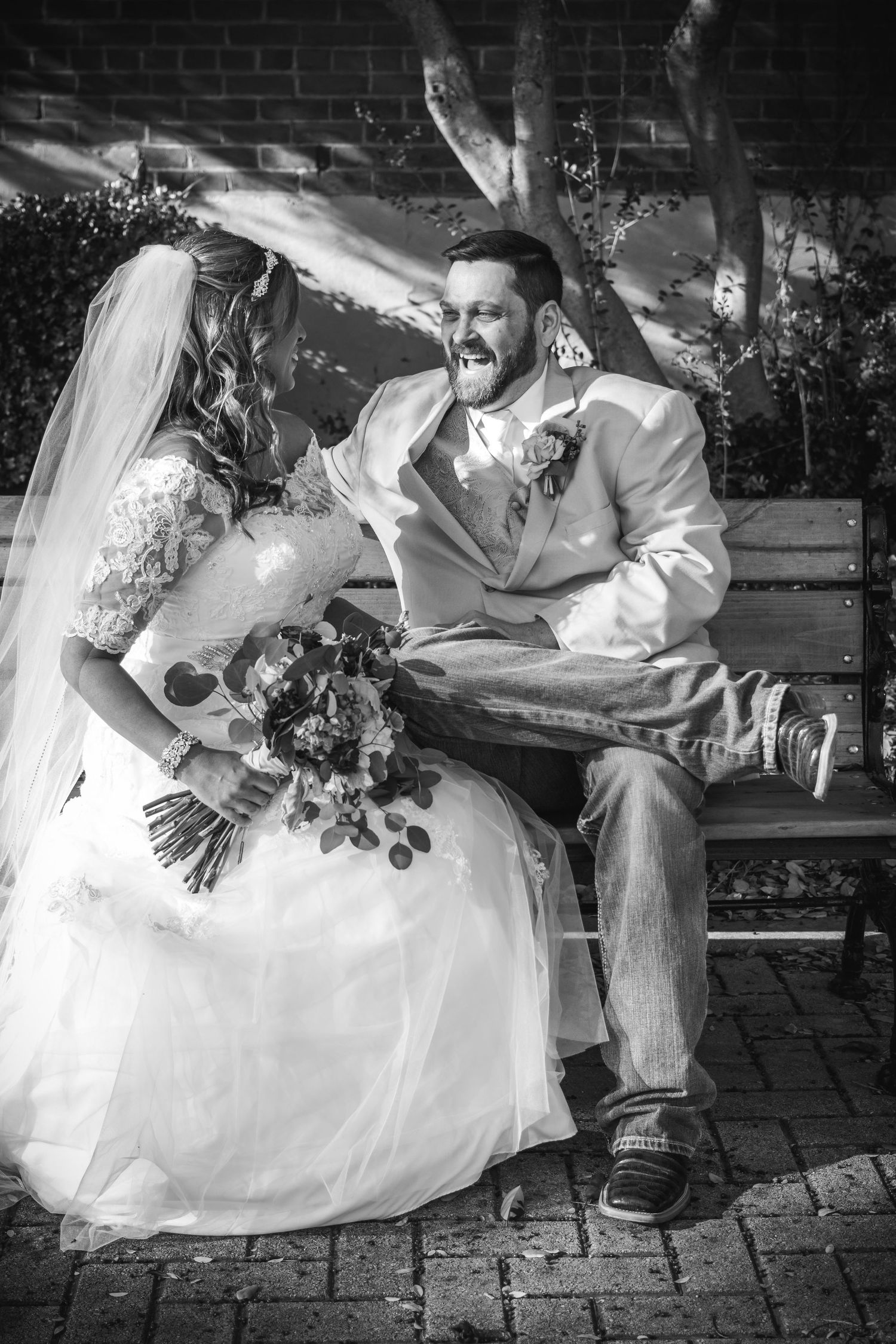 Black and white candid wedding moment captured on brick patio with floral bouquet.