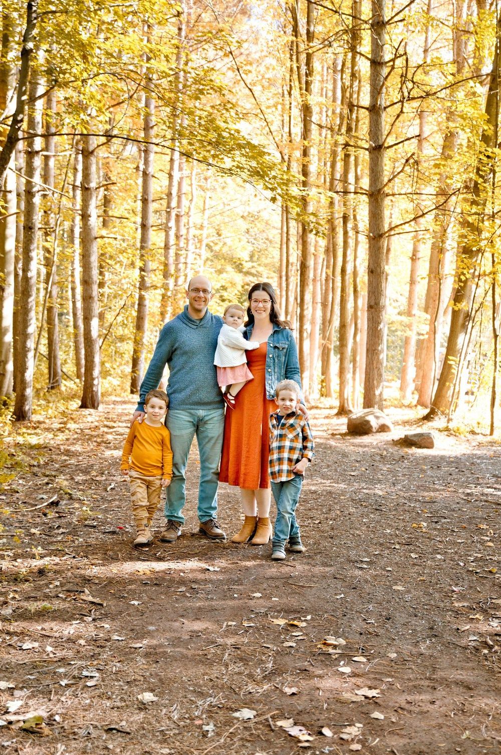 A family enjoys a sunny autumn walk together on a forest trail surrounded by golden-leaved trees.