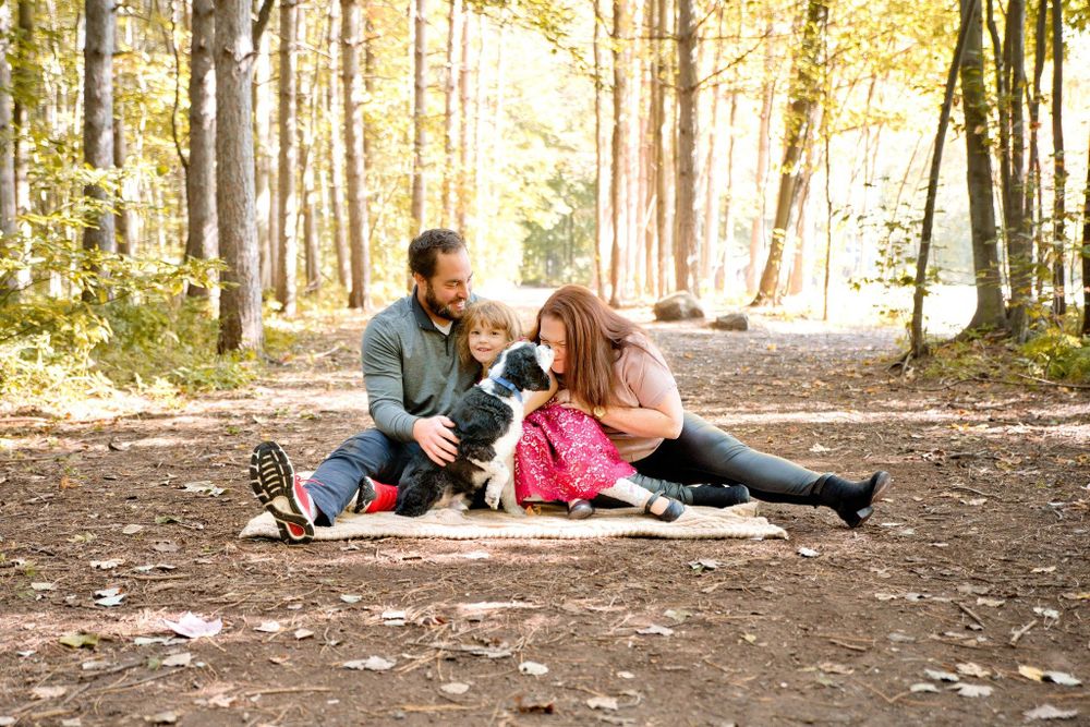 Family enjoying a picnic on a blanket in autumn woods with golden sunlight filtering through the trees.