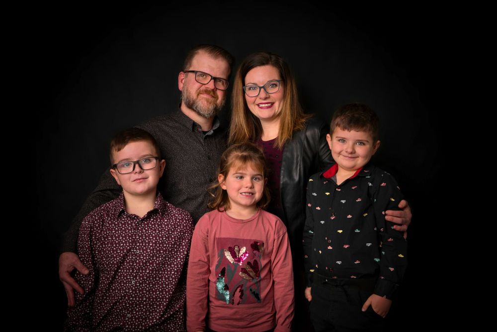 A portrait of a family posing in front of a dark background wearing casual clothing.