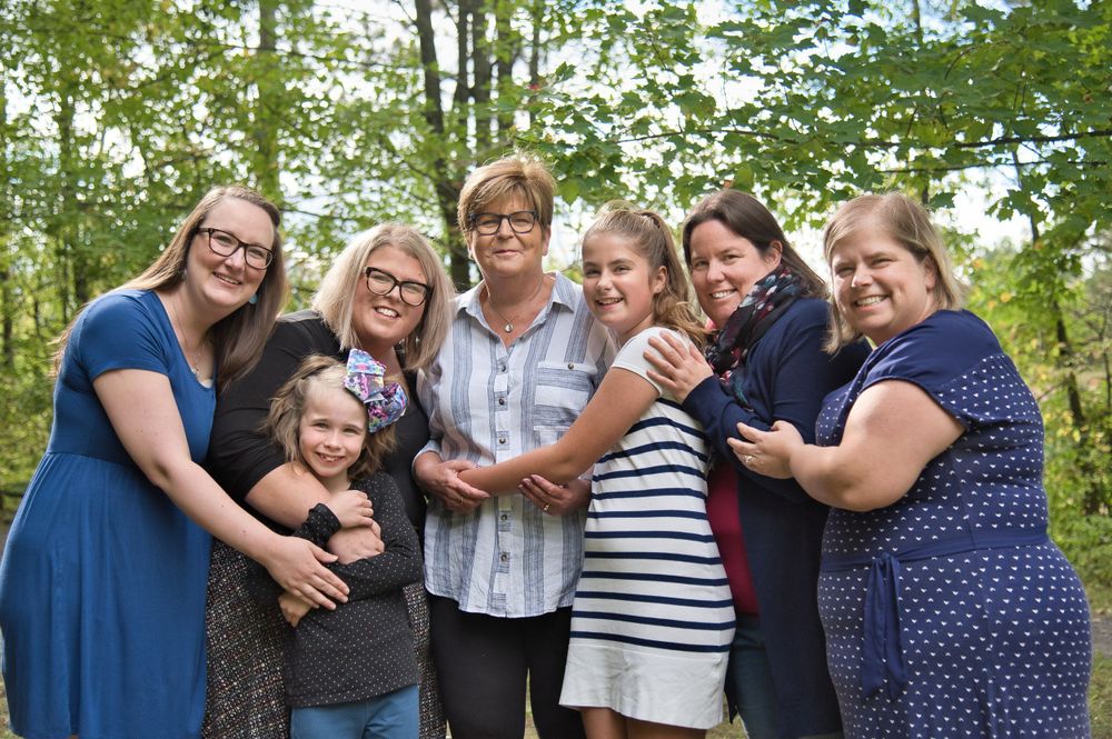 A group of people in blue and casual attire smiling and embracing while standing together outdoors in a wooded setting.