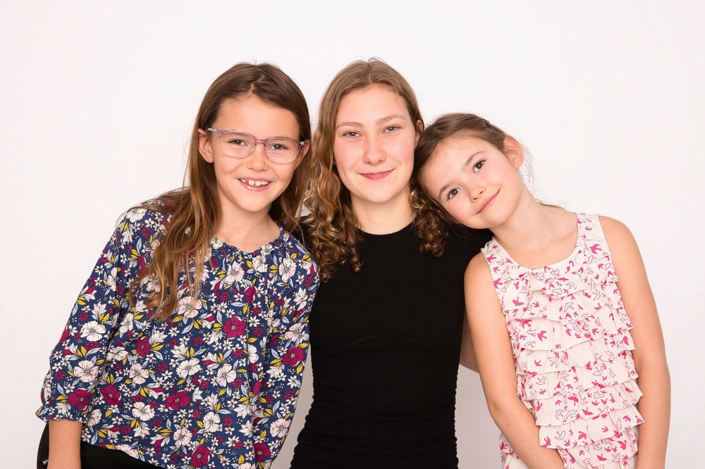 Three teens in casual attire pose together against a light background.