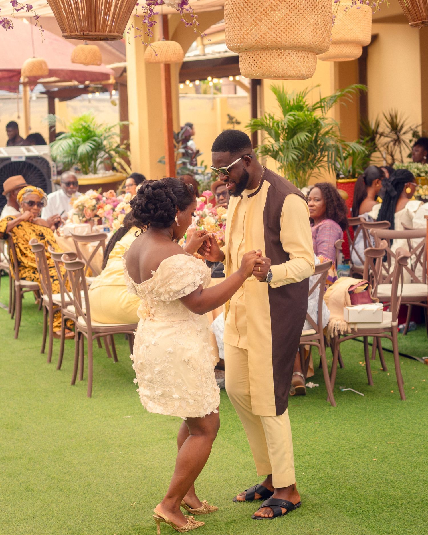 Couple in cream and white formal wear dance together on green outdoor flooring.
