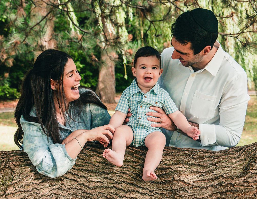 A family lies together on a large tree trunk in a wooded outdoor setting during a photo session.