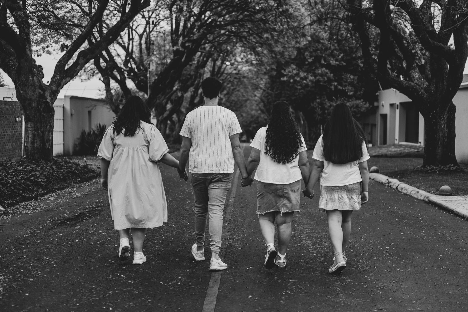 People walking together under large trees on a paved pathway in black and white.