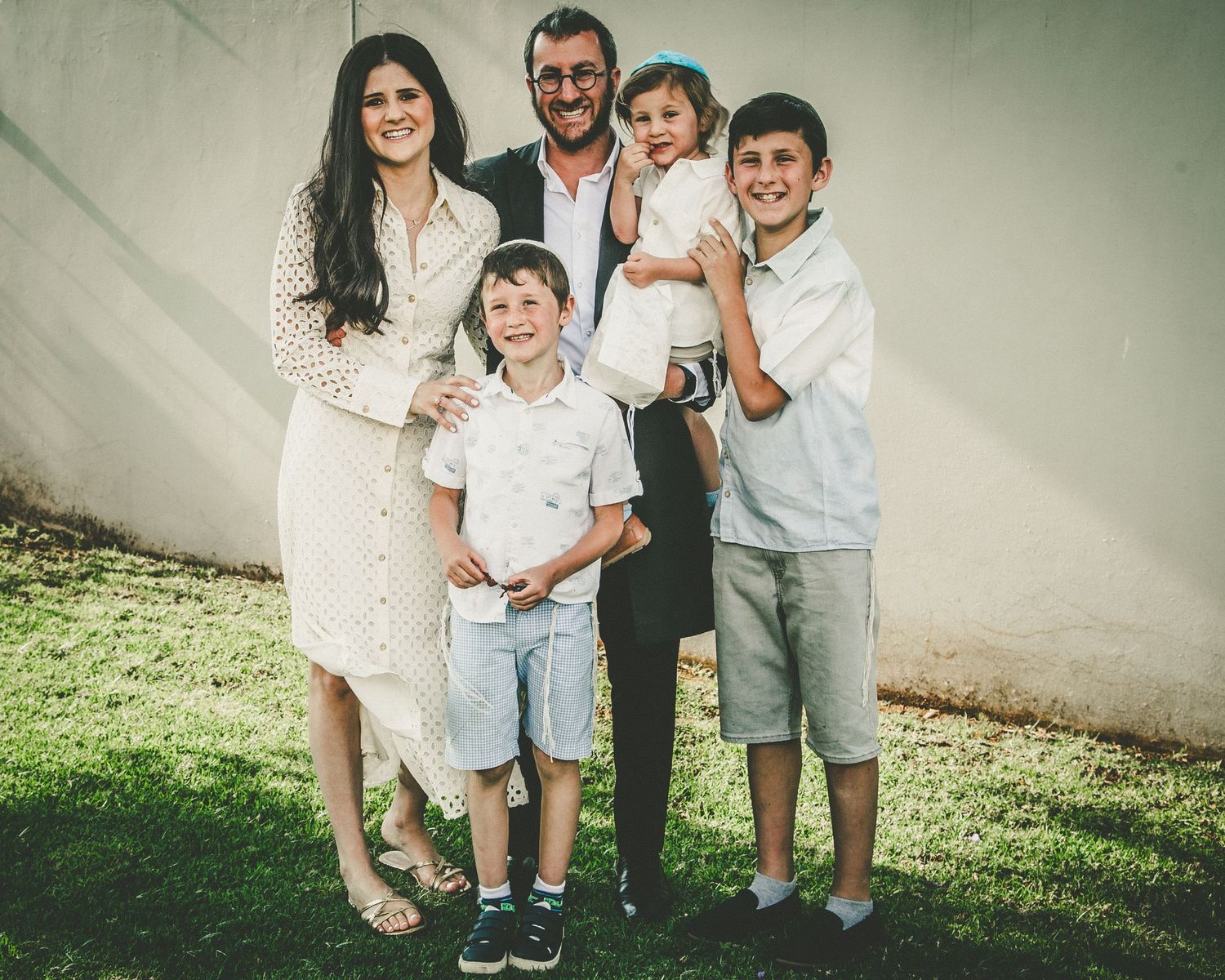 An outdoor family portrait showing parents and children posing together against a neutral wall.
