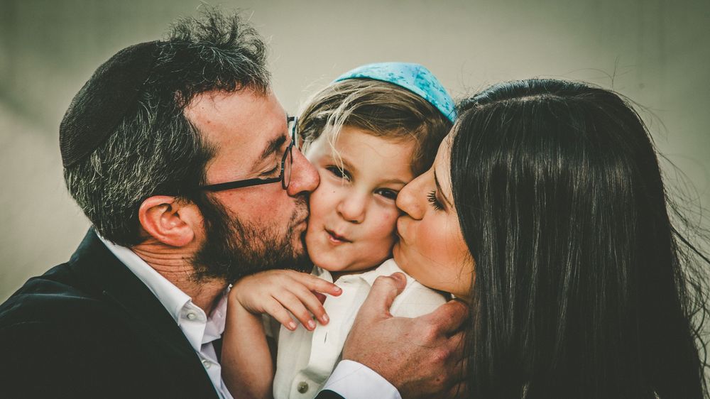 A tender family moment captured as parents share kisses with their young child in a loving embrace.