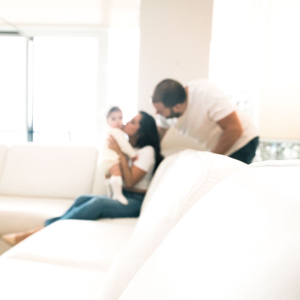 A blurry, intimate family moment captured on a white couch in a bright, minimalist living room setting.