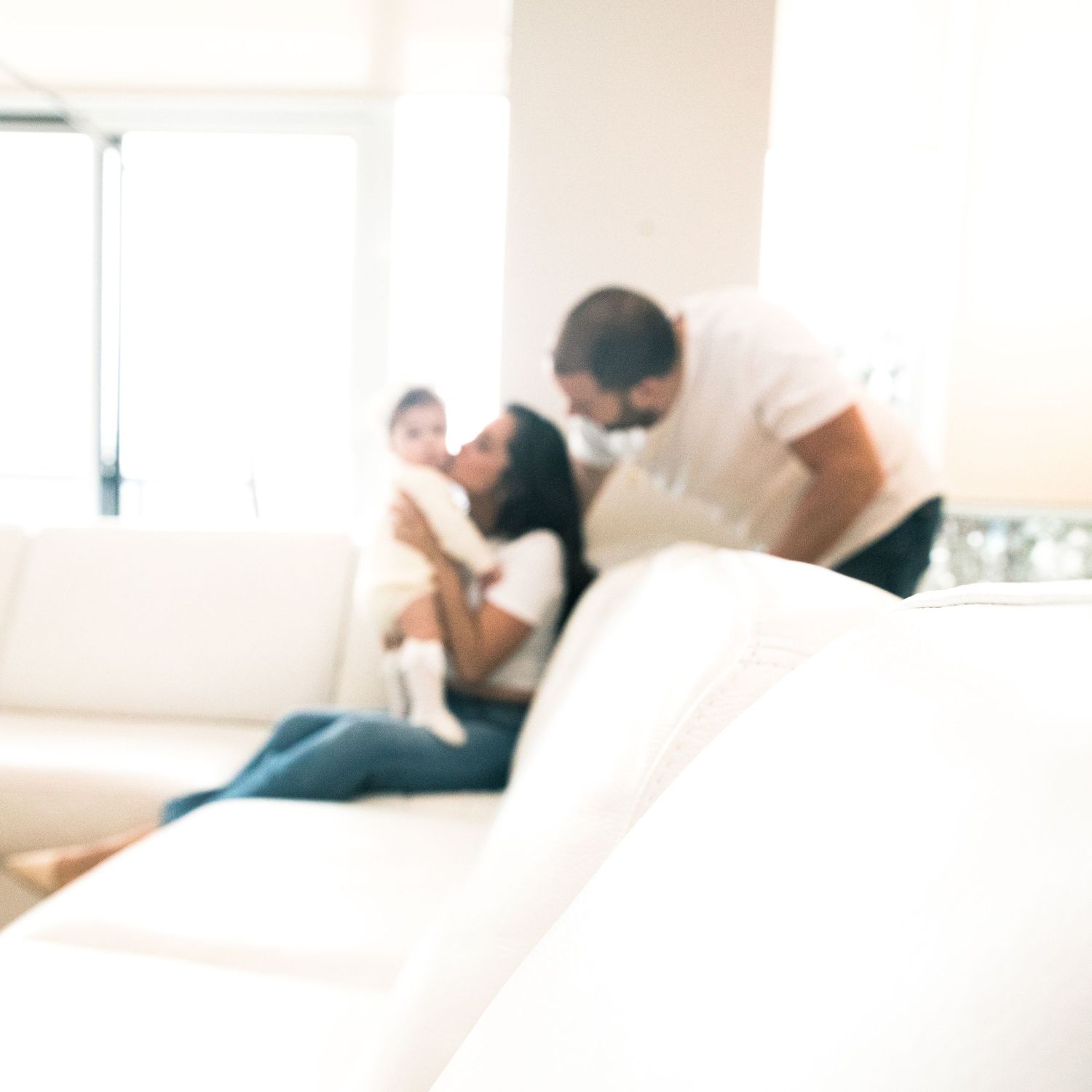 A blurry, intimate family moment captured on a white couch in a bright, minimalist living room setting.