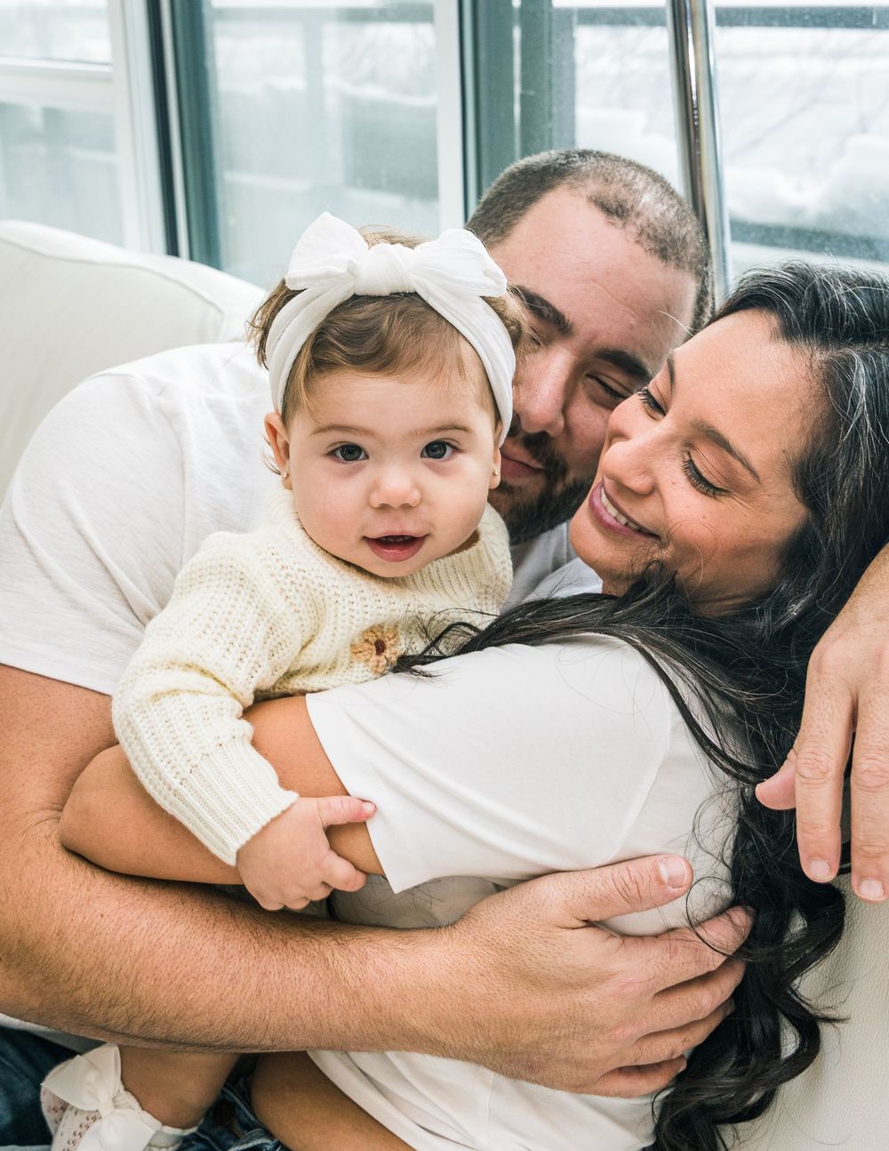 A loving family shares an intimate moment together on a couch by a window, embracing warmly in casual attire.